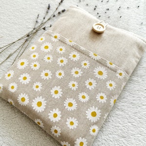 May include: A beige linen pouch with a white daisy pattern and a wooden button closure. The pouch is on a white fuzzy surface.
