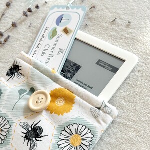 May include: A white and blue bookmark with the text "The Summer Read Club" and a floral pattern e-reader case with a bee and daisy design. The e-reader case has a button closure.