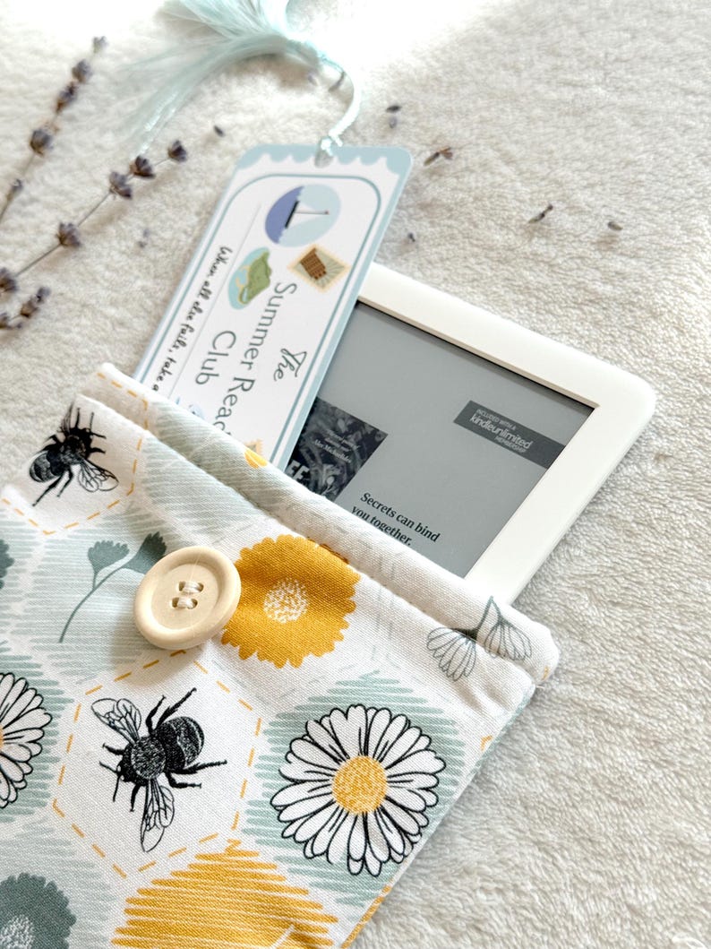 May include: A white and blue bookmark with the text "The Summer Read Club" and a floral pattern e-reader case with a bee and daisy design. The e-reader case has a button closure.