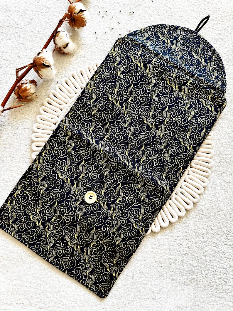 May include: A black fabric pouch with a gold cloud pattern and a single button closure. The pouch is folded in half and lying on a white surface.