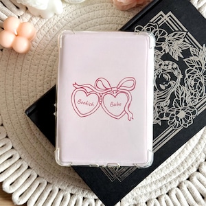 May include: A pink phone case featuring a design of two heart-shaped lockets with the words "Bookish" and "Babe" on them.