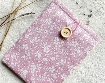 Puede incluir: Una bolsa de tela rosa con un estampado floral blanco y un cierre de botón de madera. La bolsa está sobre una superficie blanca y peluda.