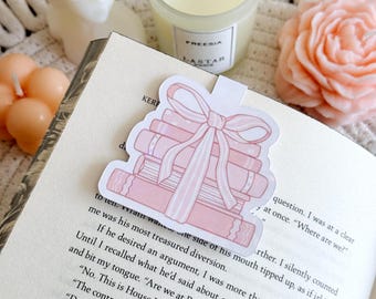 May include: A pink and white bookmark with a stack of books tied with a pink ribbon. The bookmark is on a book with the text "Where are we?" visible.