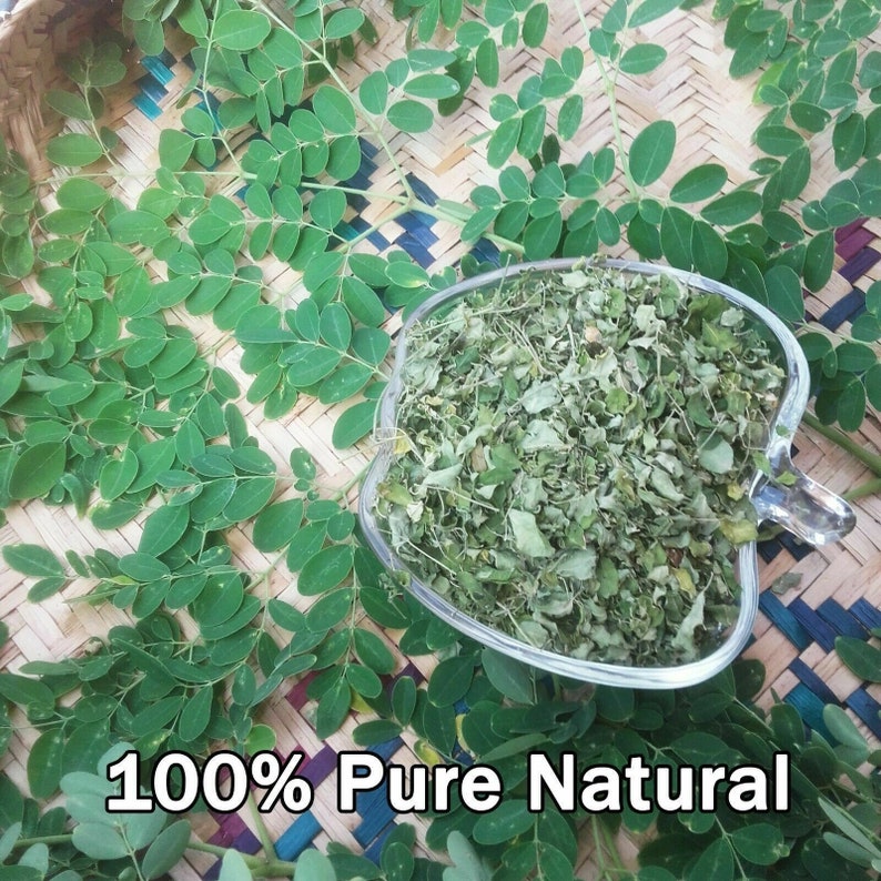 K&ouml;nnte beinhalten: Eine klare, herzf&ouml;rmige Glasschale gef&uuml;llt mit getrockneten gr&uuml;nen Bl&auml;ttern, umgeben von frischen gr&uuml;nen Bl&auml;ttern. Der Text "100% Pure Natural" ist unten im Bild zu sehen. Die Bl&auml;tter liegen auf einer gewebten Bambusmatte.
