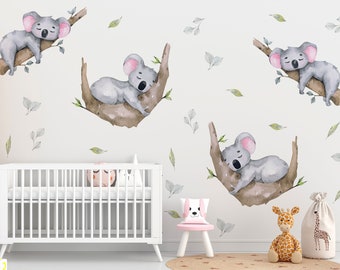 May include: A white crib with a white wooden wardrobe and a stuffed giraffe toy in a nursery with a white wall decorated with watercolor koala bear decals on branches.