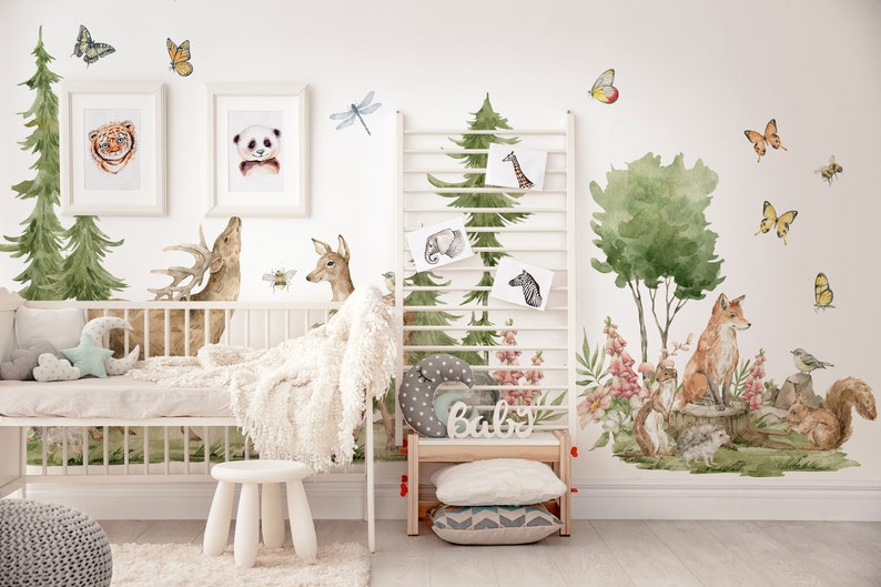 May include: A nursery room decorated with woodland animal wall decals. The decals feature a deer, a fox, a squirrel, a bird, butterflies, and trees. The room also has a white crib, a white stool, and a wooden shelf with the word "Baby" on it.