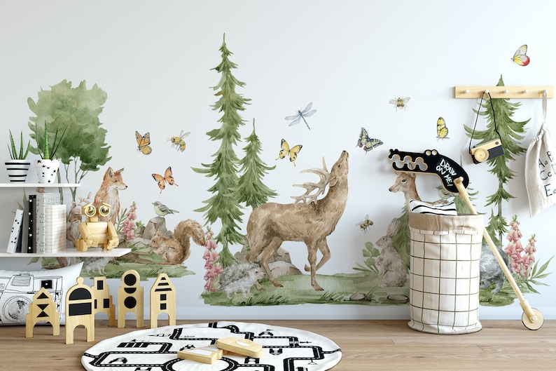 May include: A watercolor-style wall decal featuring a forest scene with a deer, fox, squirrel, and butterflies. The decal is applied to a white wall in a child's room with a wooden shelf, toys, and a black and white rug.