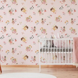 May include: Pink nursery wallpaper with a repeating pattern of fairies holding flowers and butterflies. The wallpaper is in a room with a white crib and a pink armchair.