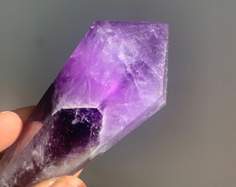 May include: A purple amethyst crystal point with a pointed tip and a smooth, polished surface.