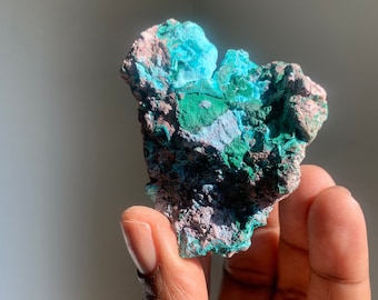 May include: A rough, green and blue gemstone with a natural, irregular shape. The gemstone has a variety of shades of green and blue, with some areas of the stone appearing more opaque than others.