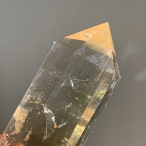 May include: A clear quartz crystal point with a golden brown hue. The crystal is faceted and has a pointed tip. The crystal is approximately 5 inches long.