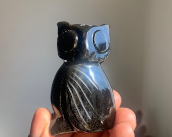 May include: Black obsidian owl figurine with gold accents. The owl is carved with detailed feathers and has large, round eyes.