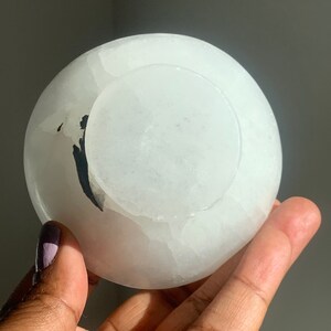May include: A white selenite bowl with a natural, rough texture. The bowl is slightly translucent and has a subtle, milky white color.