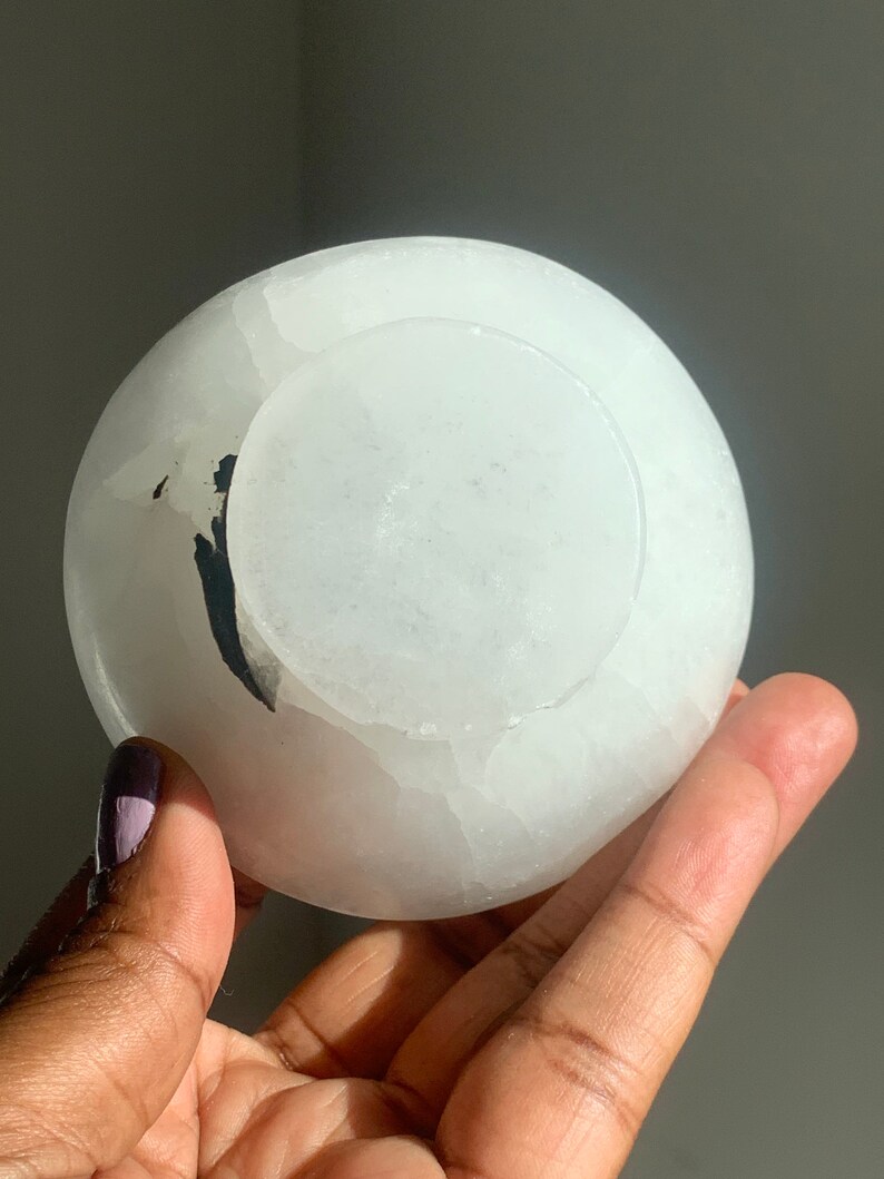 May include: A white selenite bowl with a natural, rough texture. The bowl is slightly translucent and has a subtle, milky white color.