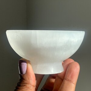 May include: A white selenite bowl with a smooth, polished surface. The bowl is shaped like a traditional bowl with a rounded base.