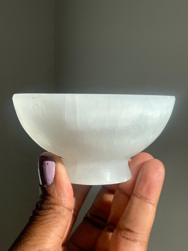 May include: A white selenite bowl with a smooth, polished surface. The bowl is shaped like a traditional bowl with a rounded base.