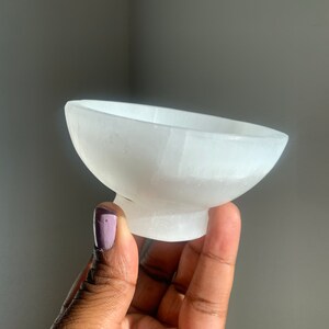 May include: A white selenite bowl with a smooth, polished surface. The bowl is shaped like a traditional bowl with a rounded base and a wide, shallow opening.
