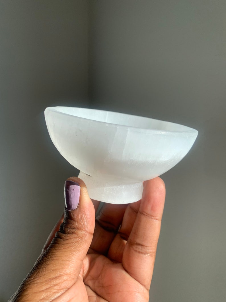 May include: A white selenite bowl with a smooth, polished surface. The bowl is shaped like a traditional bowl with a rounded base and a wide, shallow opening.