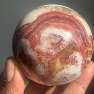 May include: A polished sphere of red, white, and brown banded agate. The sphere has a smooth, polished surface and intricate patterns.