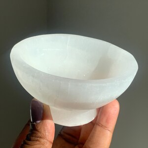 May include: A white selenite bowl with a smooth, polished surface. The bowl is shaped like a traditional bowl with a rounded base.