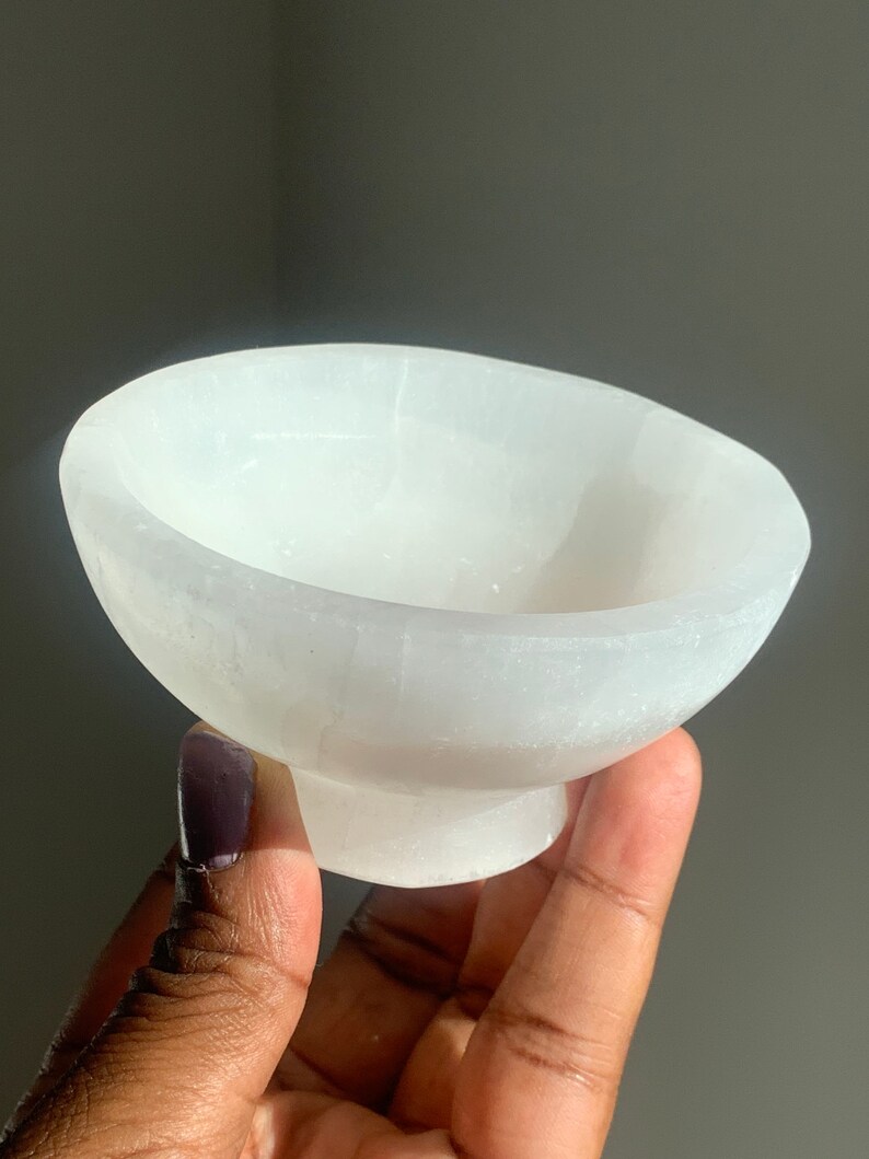 May include: A white selenite bowl with a smooth, polished surface. The bowl is shaped like a traditional bowl with a rounded base.