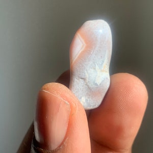 以下が含まれることがあります： ユニークな模様の白とピンクのアゲートストーン。石は滑らかで磨かれており、自然で有機的な形をしています。