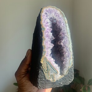 Könnte beinhalten: Ein großer Amethyst-Geode mit einem tiefvioletten Inneren und einem schwarzen Äußeren. Der Geode ist teilweise geöffnet und zeigt die Kristalle im Inneren.
