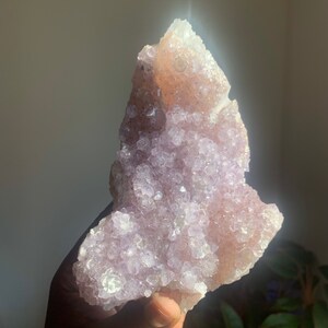Könnte beinhalten: Ein großer, violetter Amethyst-Cluster mit einer rauen, strukturierten Oberfläche. Der Kristall ist hellviolett und hat eine natürliche, organische Form.