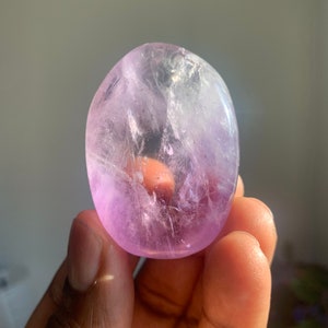 Könnte beinhalten: Ein glatter, ovaler Amethyst-Kristall mit einer hellvioletten Farbe. Der Kristall ist durchscheinend und hat eine natürliche, polierte Oberfläche.