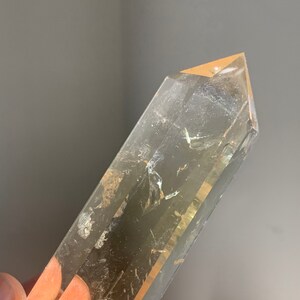 May include: A clear quartz crystal point with a golden hue. The crystal is long and slender with a pointed tip. It has a natural, raw look.