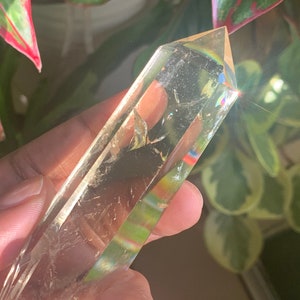 May include: A clear quartz crystal point with a rainbow effect. The crystal is held in a hand.