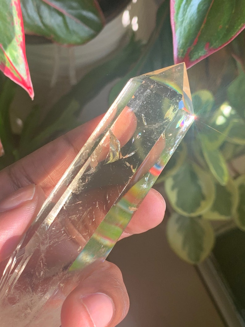May include: A clear quartz crystal point with a rainbow effect. The crystal is held in a hand.