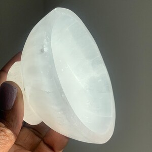 May include: A white selenite bowl with a smooth, polished surface. The bowl is slightly curved and has a rounded base.