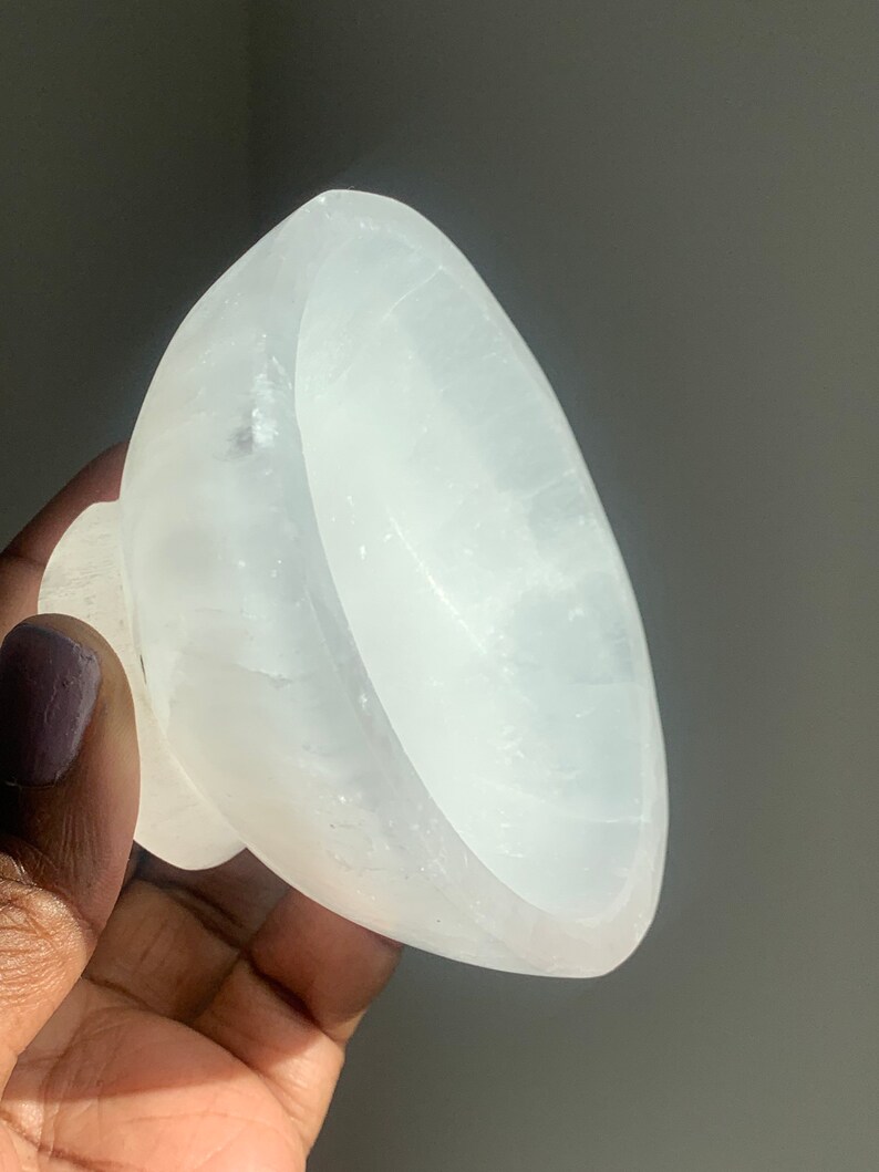 May include: A white selenite bowl with a smooth, polished surface. The bowl is slightly curved and has a rounded base.