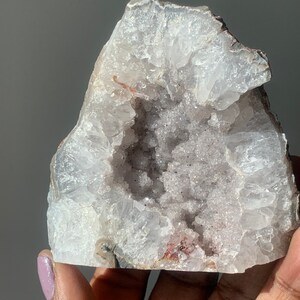 K&ouml;nnte beinhalten: Ein wei&szlig;er Achat-Geode mit einer gro&szlig;en &Ouml;ffnung, die einen Cluster kleinerer Kristalle freilegt. Der Geode hat ein raues, nat&uuml;rliches &Auml;u&szlig;eres und ein glattes, poliertes Inneres.