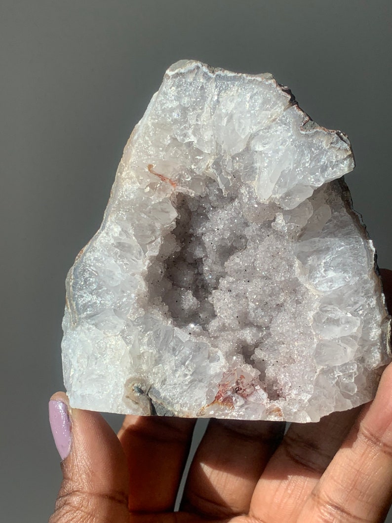 K&ouml;nnte beinhalten: Ein wei&szlig;er Achat-Geode mit einer gro&szlig;en &Ouml;ffnung, die einen Cluster kleinerer Kristalle freilegt. Der Geode hat ein raues, nat&uuml;rliches &Auml;u&szlig;eres und ein glattes, poliertes Inneres.