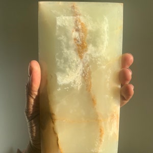 Puede incluir: Una pieza grande y rectangular de ónix verde con vetas marrones. La piedra tiene una superficie lisa y pulida.