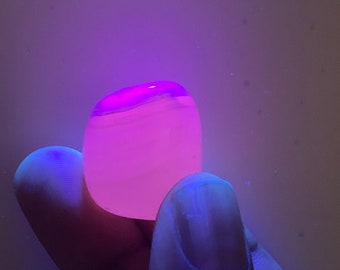 May include: A smooth, round, pink stone with white swirls, glowing under a UV light.