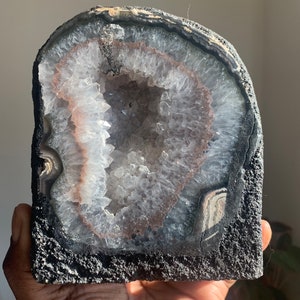 Könnte beinhalten: Eine große, natürliche Achat-Geode mit schwarzer Außenseite und weißem, kristallbesetztem Inneren. Die Geode ist teilweise geöffnet und zeigt die Kristalle im Inneren.