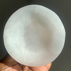 May include: A white selenite bowl, a smooth, polished, and naturally occurring crystal, with a slightly rounded shape. The bowl is approximately 4 inches in diameter.