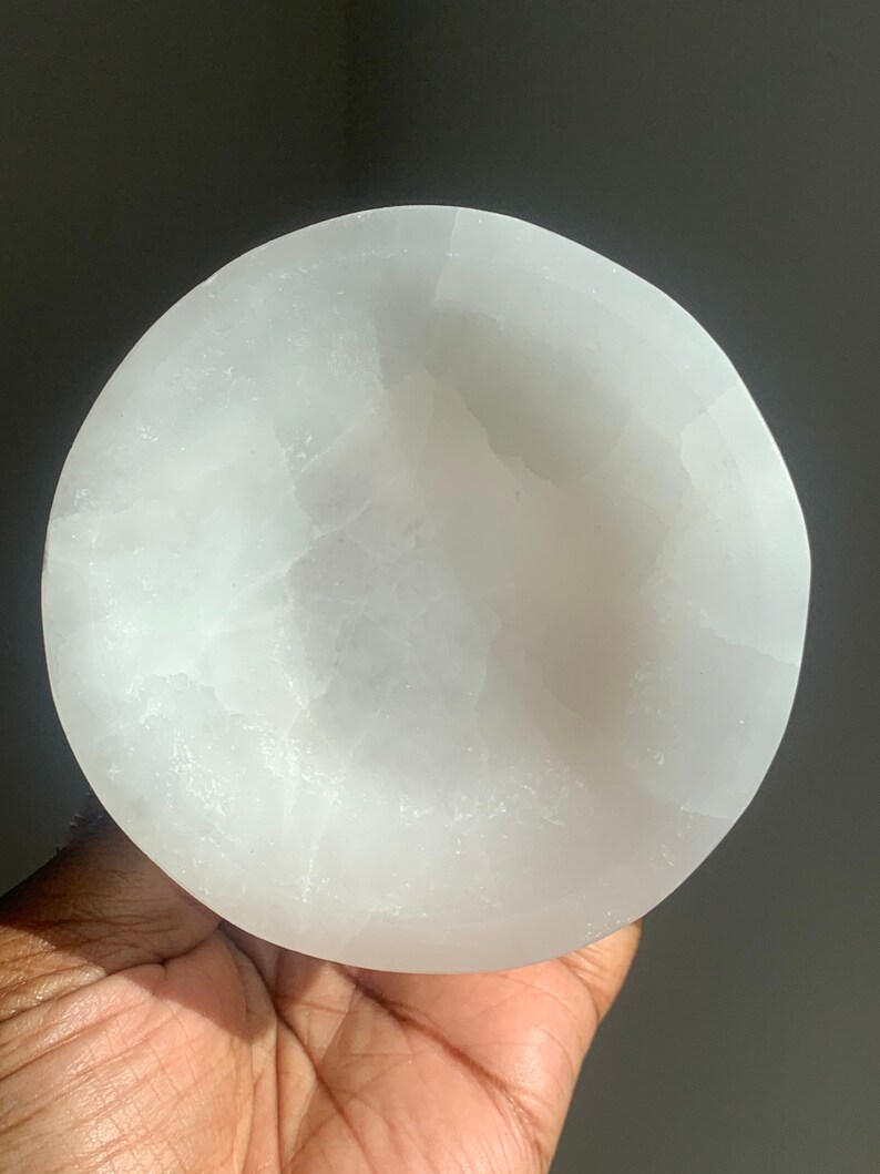 May include: A white selenite bowl, a smooth, polished, and naturally occurring crystal, with a slightly rounded shape. The bowl is approximately 4 inches in diameter.