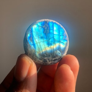 May include: A round, smooth, polished labradorite stone with iridescent blue and green colors.