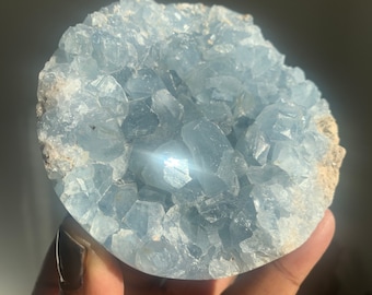 May include: A large, light blue celestite crystal cluster with a smooth, rounded surface. The crystal is composed of many small, individual crystals that are tightly packed together.