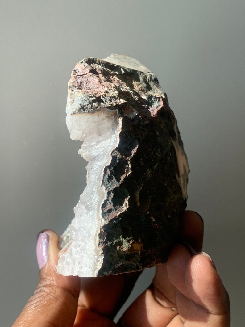 K&ouml;nnte beinhalten: Eine gro&szlig;e, wei&szlig;e Kristallgeode mit einer rauen, braunen und grauen Au&szlig;enseite. Die Geode ist teilweise ge&ouml;ffnet und zeigt die wei&szlig;en Kristalle im Inneren.