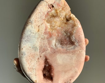 May include: A large, pink and white geode with a natural, irregular shape. The geode has a large, open cavity filled with smaller, white crystals.