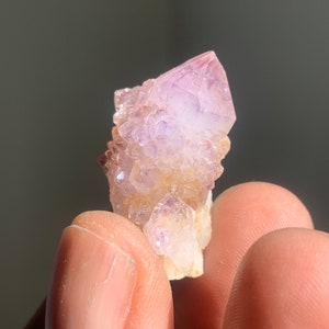 Könnte beinhalten: Ein kleiner Cluster aus Amethyst-Kristallen in violetter und weißer Farbe. Die Kristalle sind in einer natürlichen Formation zusammengefügt.