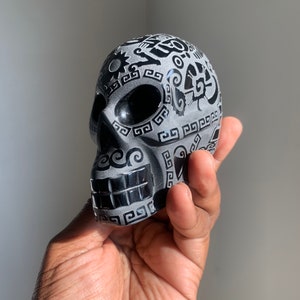 May include: A black and white sugar skull with intricate designs. The skull is made of ceramic and has a glossy finish.