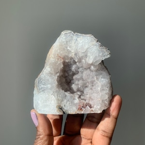 K&ouml;nnte beinhalten: Eine wei&szlig;e und violette Amethyst-Geode mit einer gro&szlig;en &Ouml;ffnung, die die Kristallformationen im Inneren freilegt.