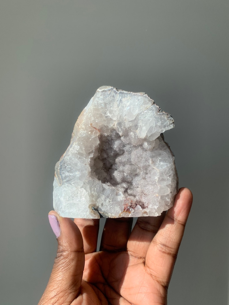 K&ouml;nnte beinhalten: Eine wei&szlig;e und violette Amethyst-Geode mit einer gro&szlig;en &Ouml;ffnung, die die Kristallformationen im Inneren freilegt.