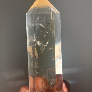 May include: A clear quartz crystal point with a light brown tip. The crystal is faceted and has a smooth, polished finish.